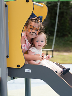 Children get read to slide down at a playground slide. One older girl has her face painted like a tiger.